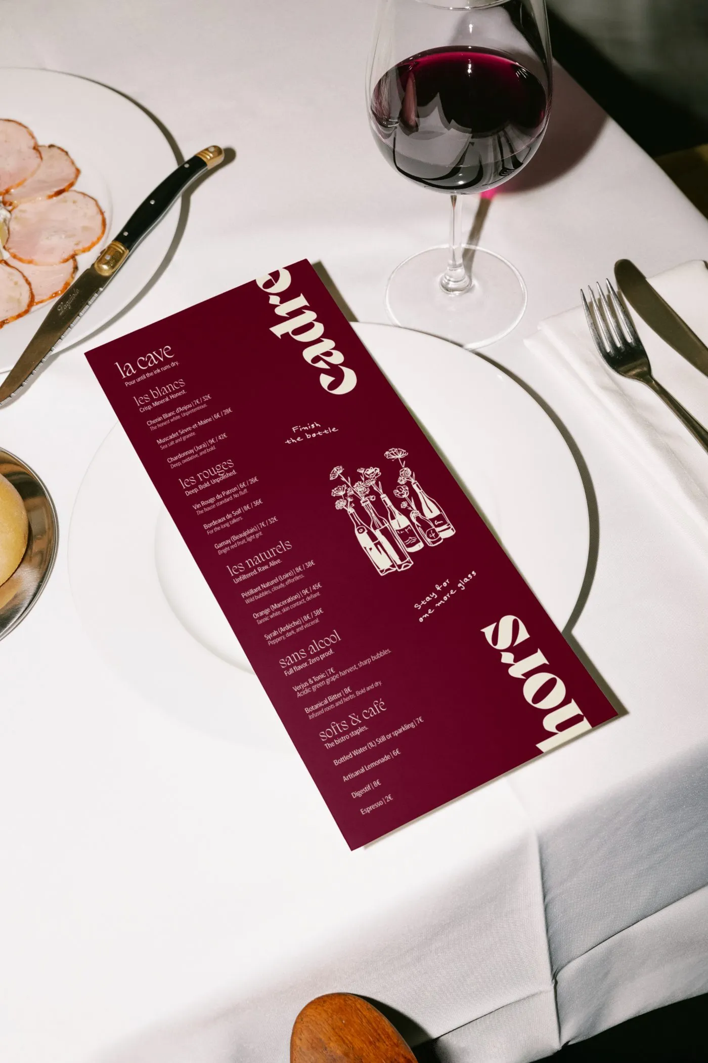 Hors Cadre wine list, la cave, on a white plate beside a glass of red